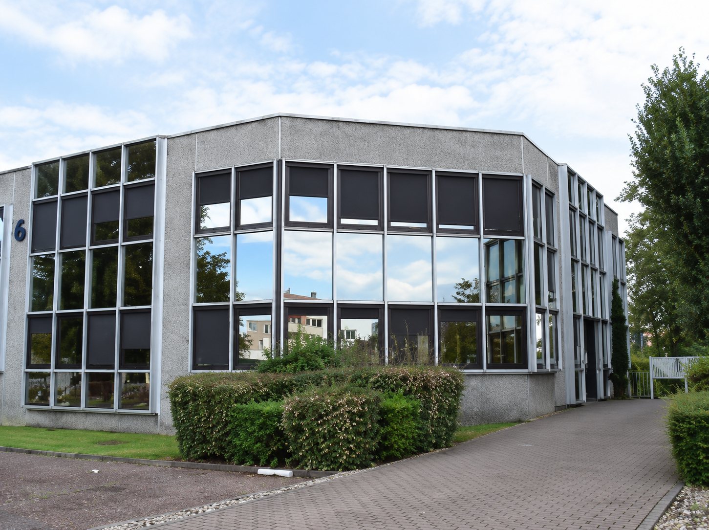 Bâtiment du cabinet, grandes baies vitrées donnant sur une allée pavée et des haies